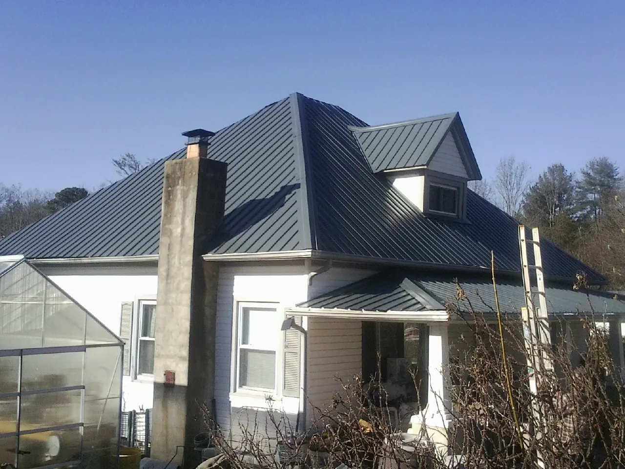 Dark blue standing seam metal roof on a white farmhouse with dormer — Slate & Tile Roof Repair by Roofing Brothers in Pratt