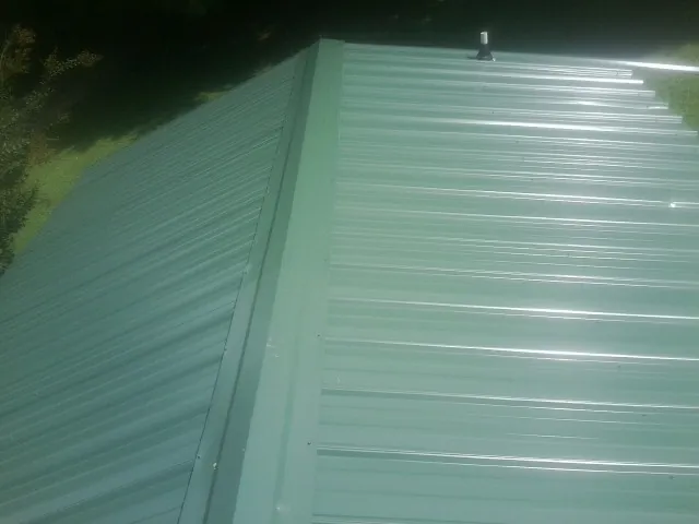 New green metal panels meeting at the ridge of a roof — Flat Roof Repair work by our crew in Pratt