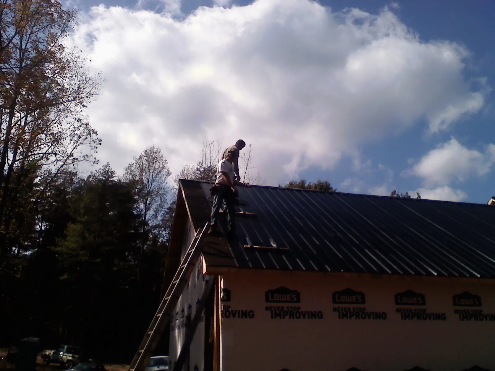 Roofer fastening dark metal panels high against a cloudy sky, from a Roof Inspection job in Pratt