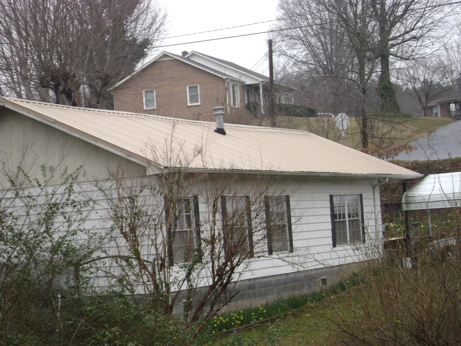 Tan metal roof on a white sided house set into a hillside — Commercial Roofing by Roofing Brothers in Pratt