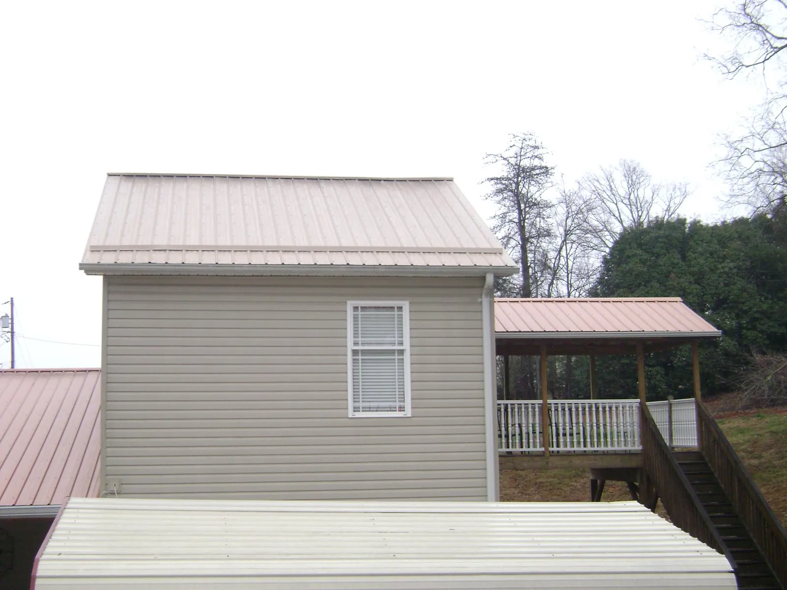 Tan metal roofs on a two story addition and attached porch, from a Roof Replacement job in Pratt